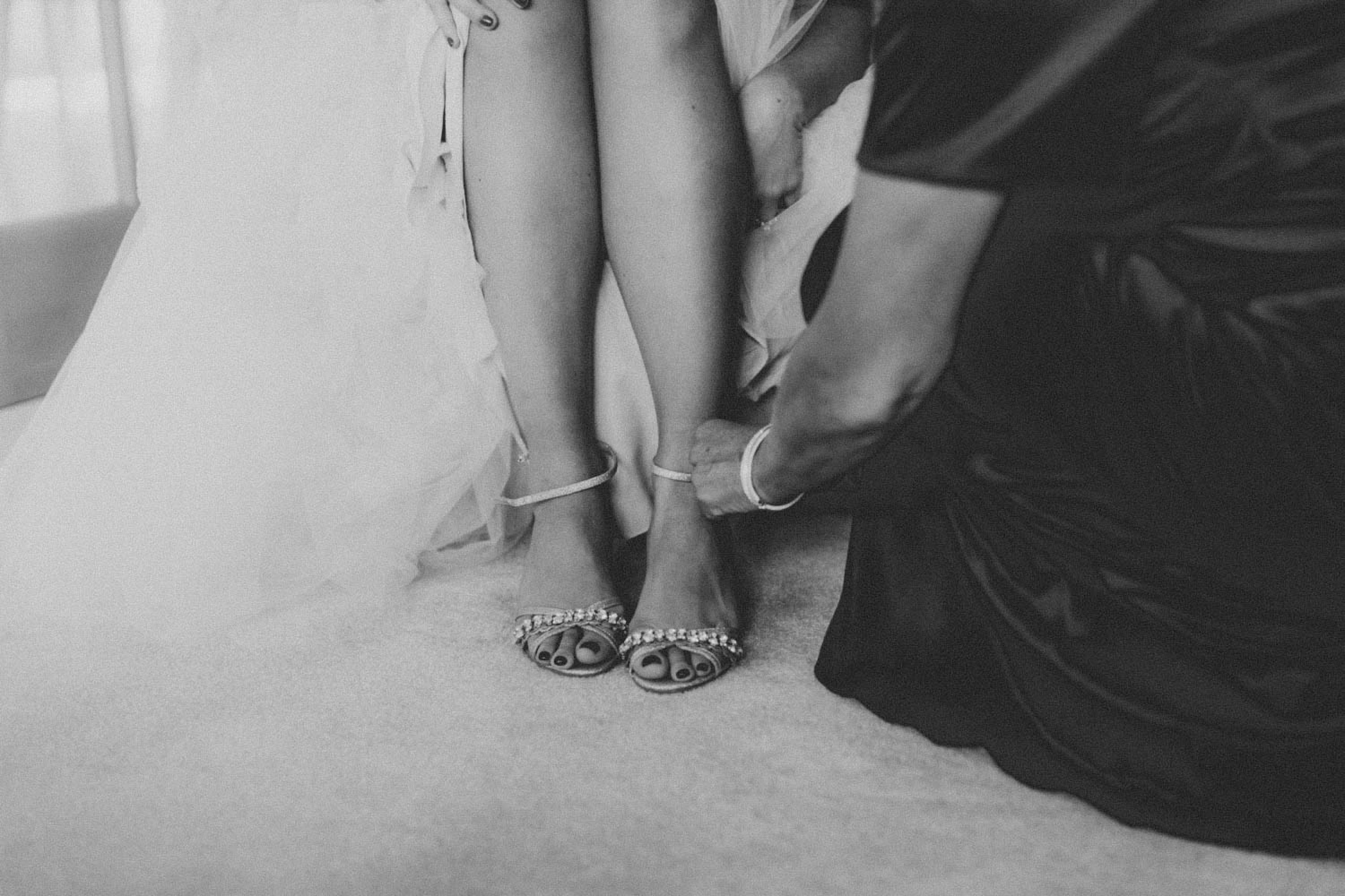 Someone fastening the strap of the bride’s shoe before the ceremony