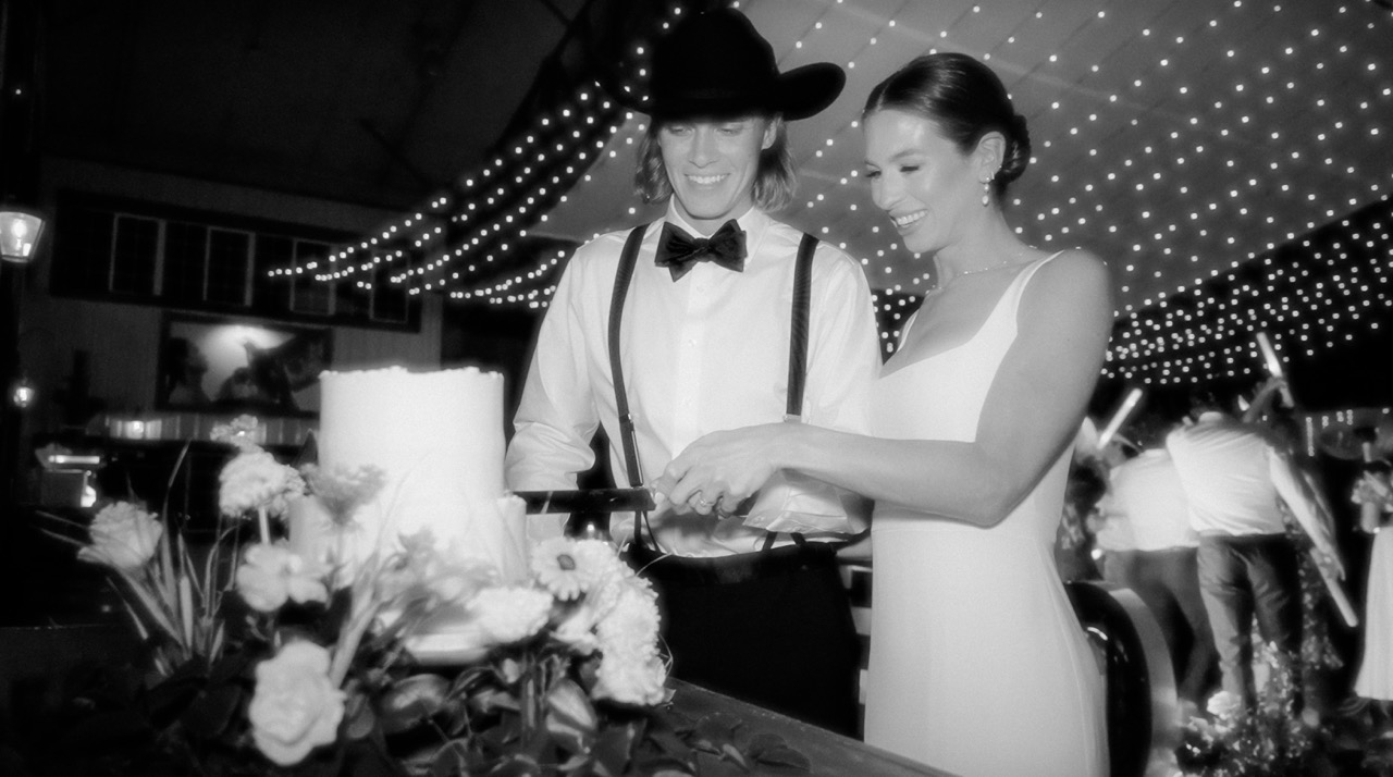 A couple cutting their wedding cake beneath strings of lights