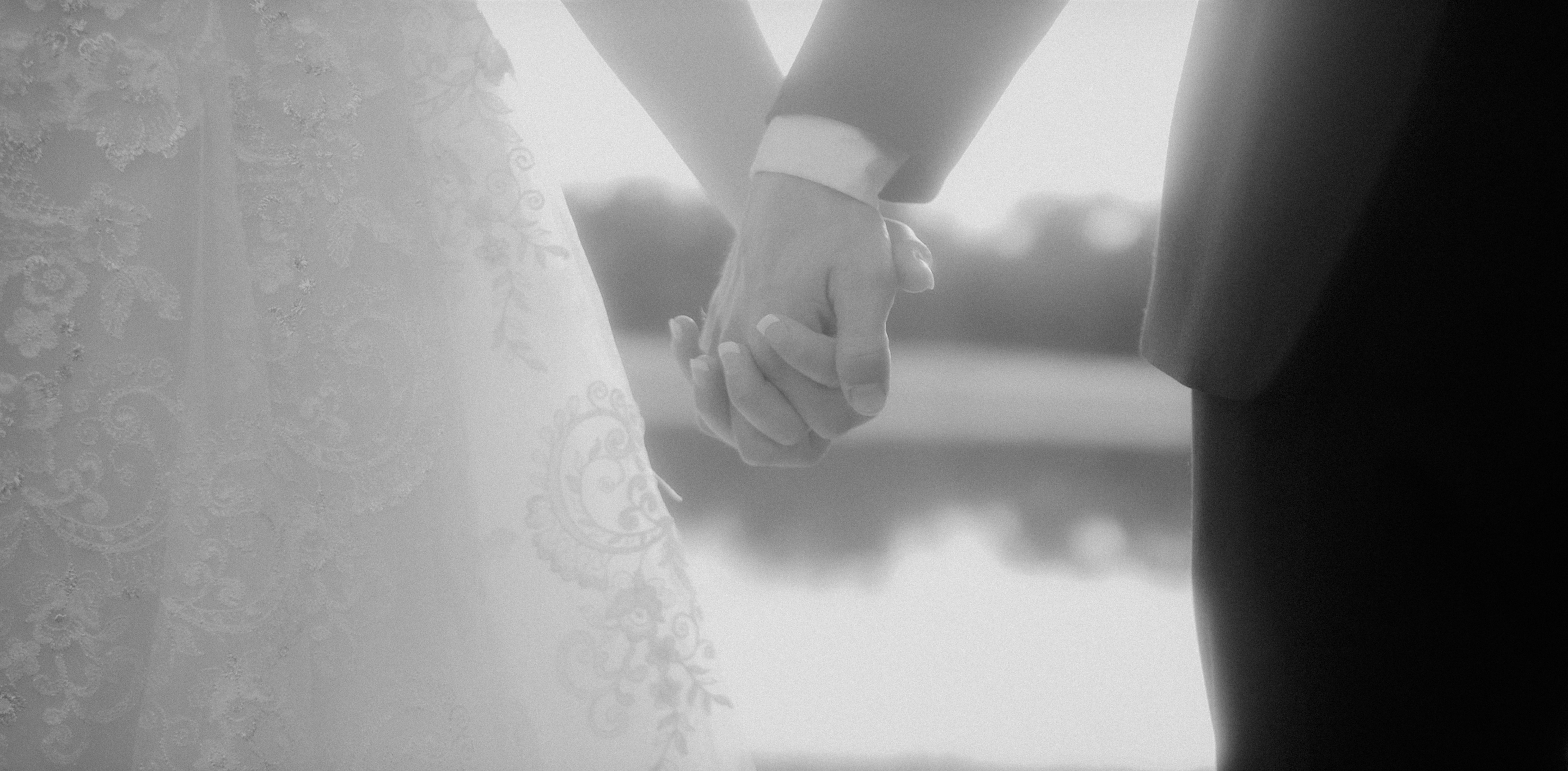 A bride and groom holding hands, photographed close, with water behind them