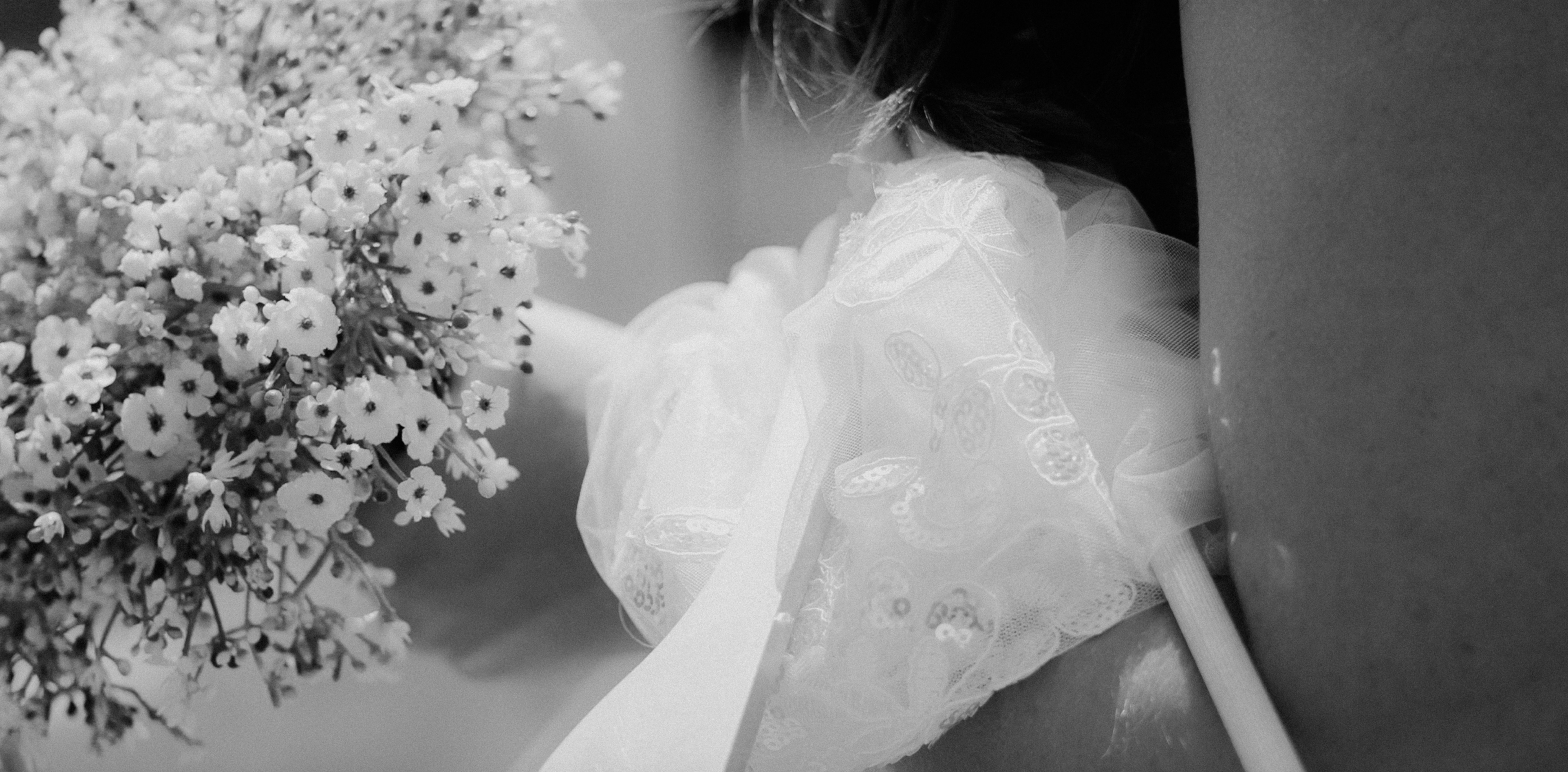A bouquet of small white flowers held beside a lace wedding dress