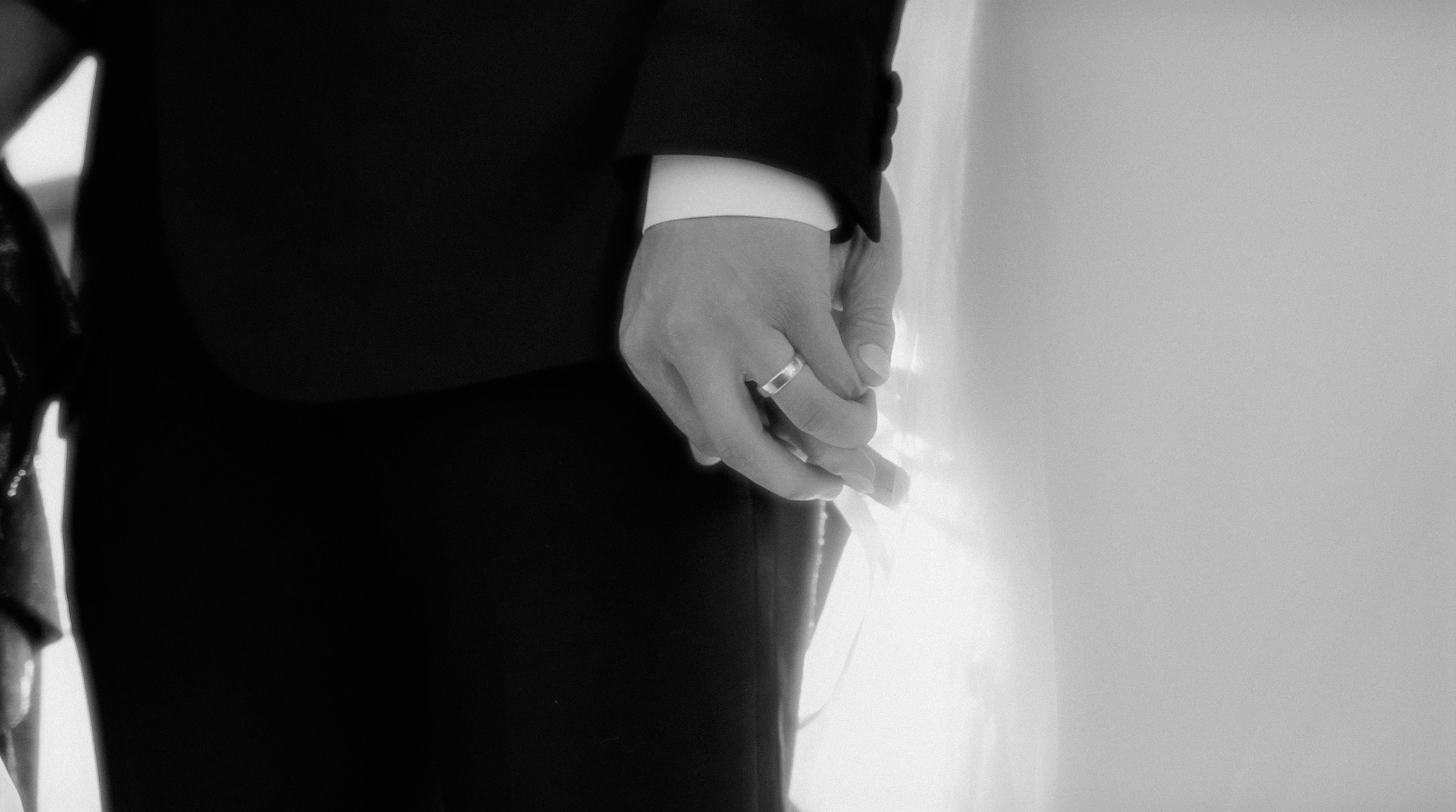 A groom’s hand, wearing his ring, resting beside the bride’s dress