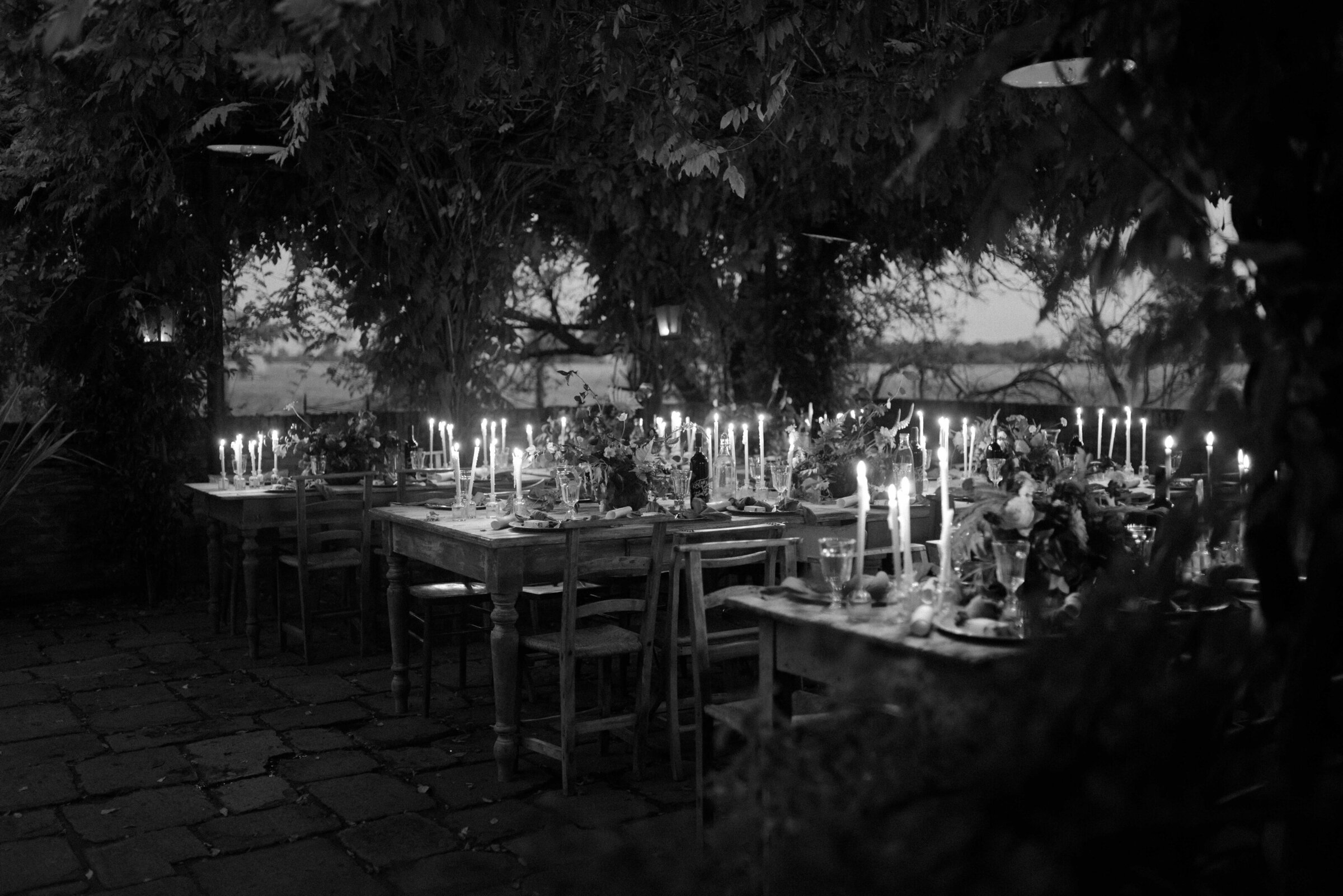 Long tables laid with candles under the trees, set for a wedding dinner